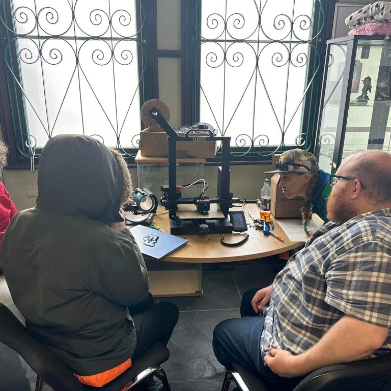 Three individuals engaged in discussion around a table with equipment in a bright room.
