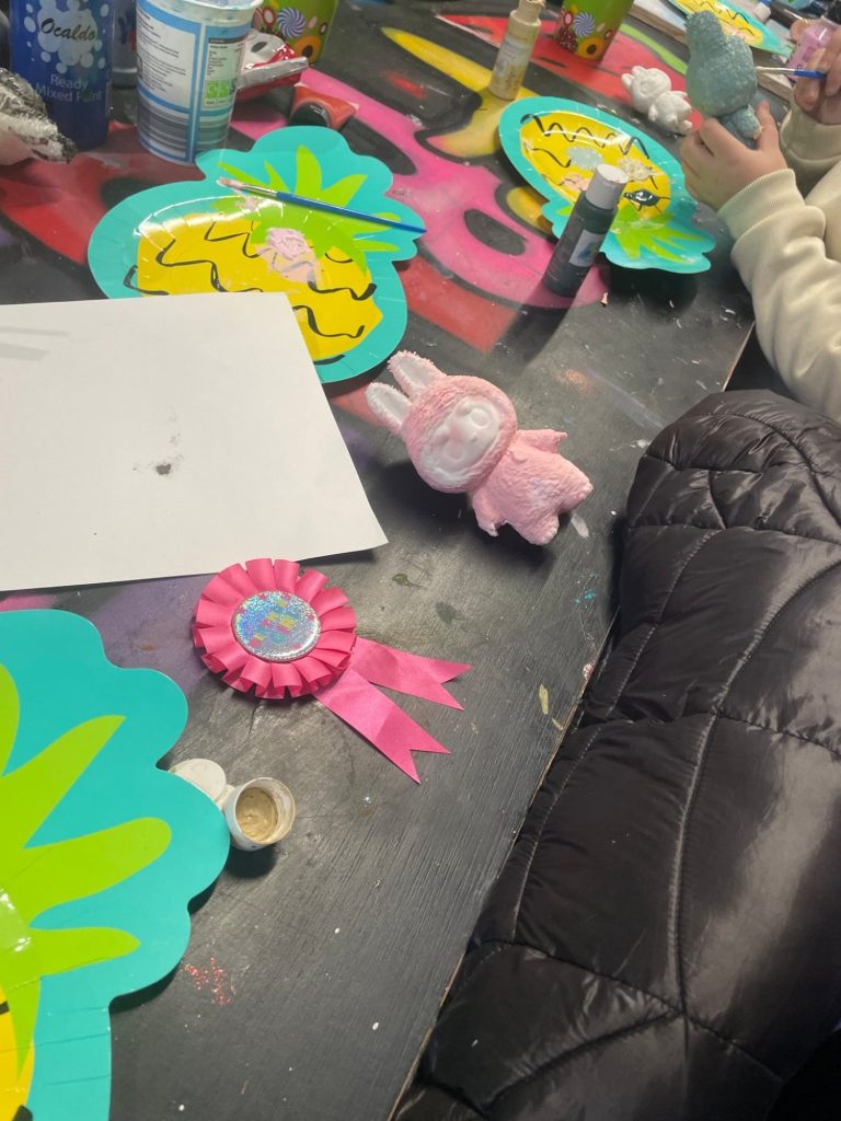 Crafting materials on a table, including painted items and a pink labubu.